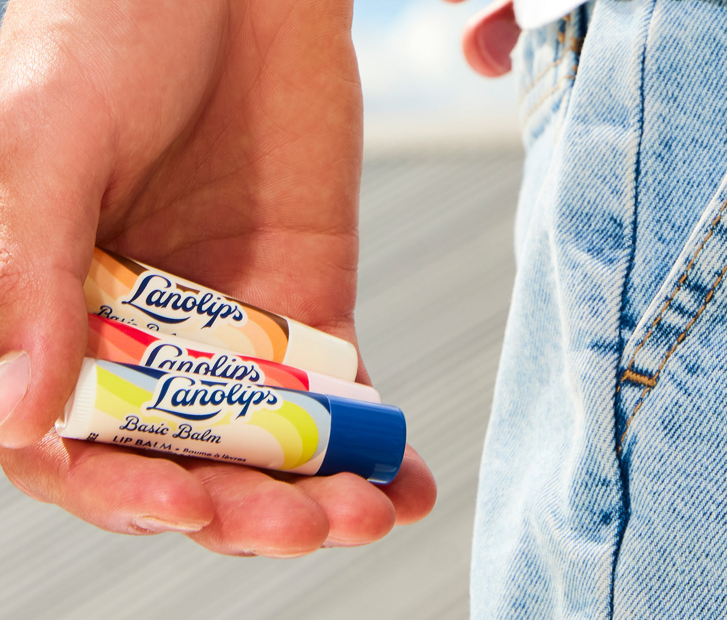 Model holding lanolips basic balm vanilla, strawberry and coconut flavours in his hand 
